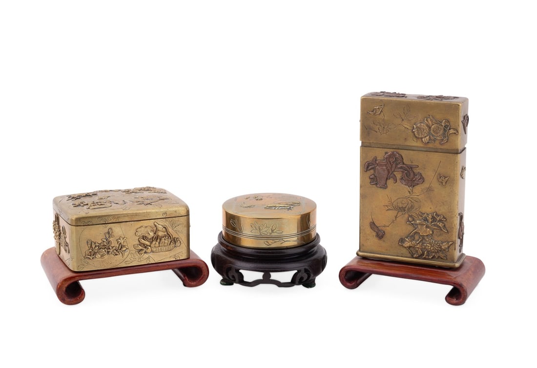 THREE JAPANESE DECORATIVE METALWORK BOXES: Japanese, likely Meiji period. Three small mixed-metal decorative boxes, comprising a rectangular box cast with auspicious symbols and floral motifs, apparently unmarked; a cylindrical box with incise