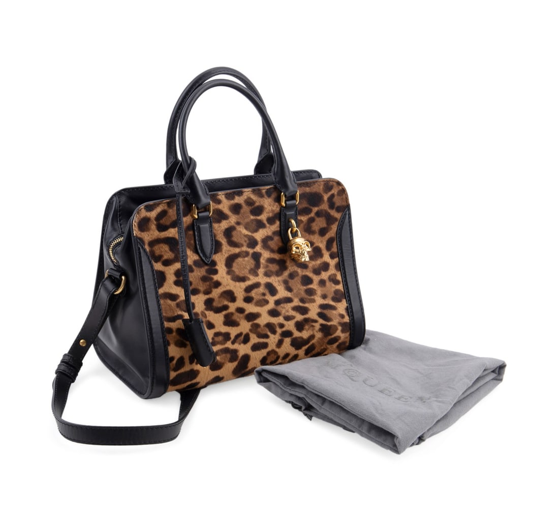 ALEXANDER MCQUEEN LEOPARD PRINT SKULL PADLOCK TOTE: Alexander McQueen (British, founded 1992). Leopard print and black leather tote, having pony hair, gold tone hardware, skull pad lock, two keys, and a cross body strap. Stamped maker's marks and seria