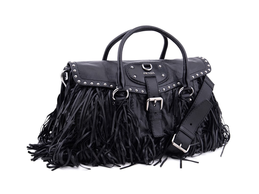 PRADA BLACK VITELLO SHINE LEATHER FRINGE FLAP BAG: Prada (Italian, founded 1913). Black vitello shine leather bag with fringe, front flap closure with buckle, silver toned hardware and studs, and two top handles. Accompanied by removable crossbody str