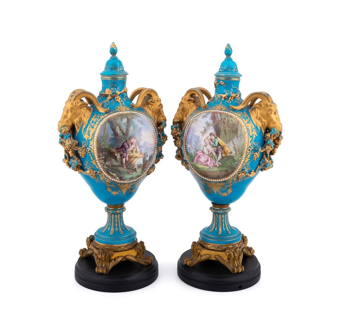 PR. OF SEVRES LOUIS XVI REVIVAL BLEU CELESTE URNS: Sevres Manufactory (French, founded 1740), mid-19th century. Pair of Louis XVI Revival bleu celeste lidded porcelain urns, each having double rams' heads, figural and floral reserves, and rising on so