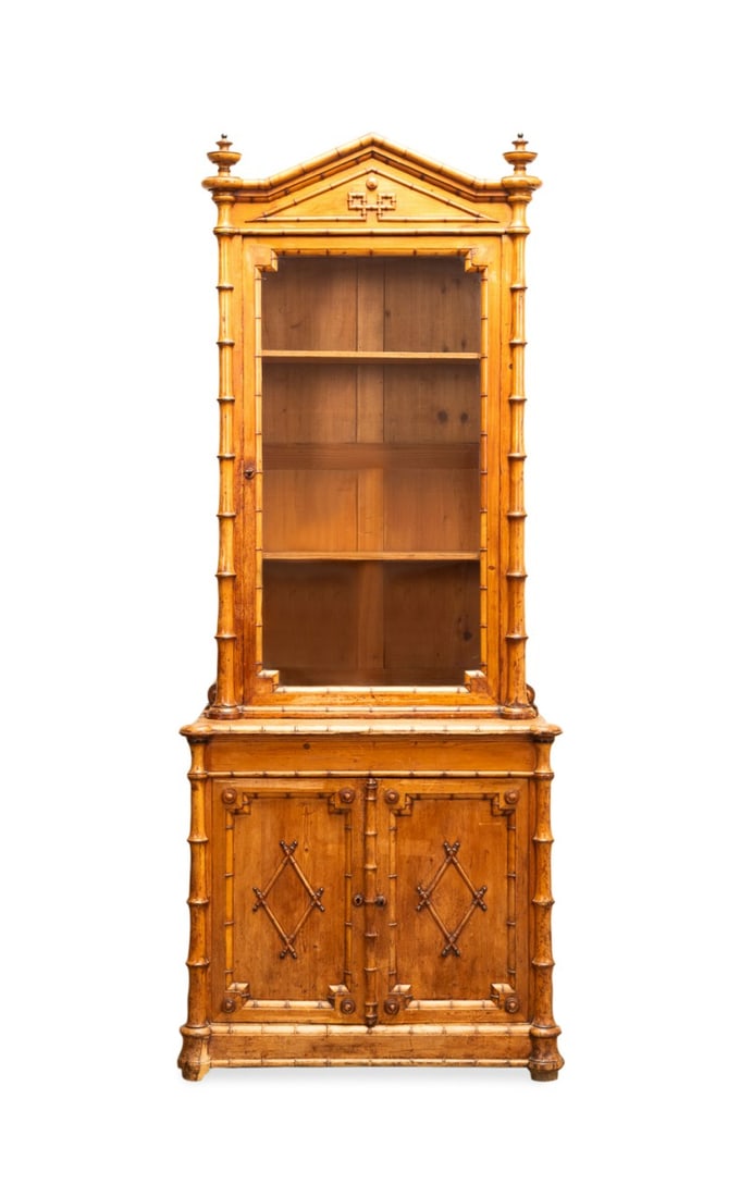 VICTORIAN AESTHETIC MOVEMENT FAUX BAMBOO VITRINE: French, last half 19th century. Victorian Aesthetic Movement faux bamboo gun cabinet, now fitted as a vitrine, having a pediment flanked by urns, single glazed door, double paneled doors, and rising o
