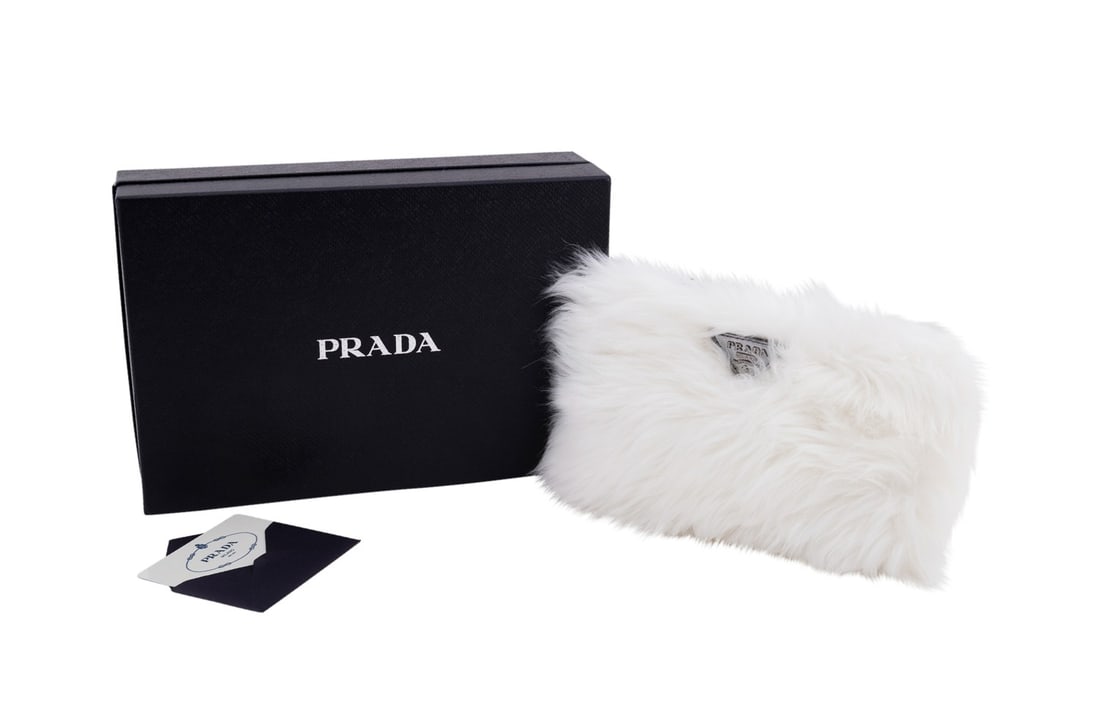 PRADA WHITE FAUX FUR WRISTLET CLUTCH: Prada (Italian, founded 1913). White faux fur wristlet clutch with metallic silver trim and triangle logo, zip top closure, and satin lining. Accompanied by box and authenticity card. Approximate meas