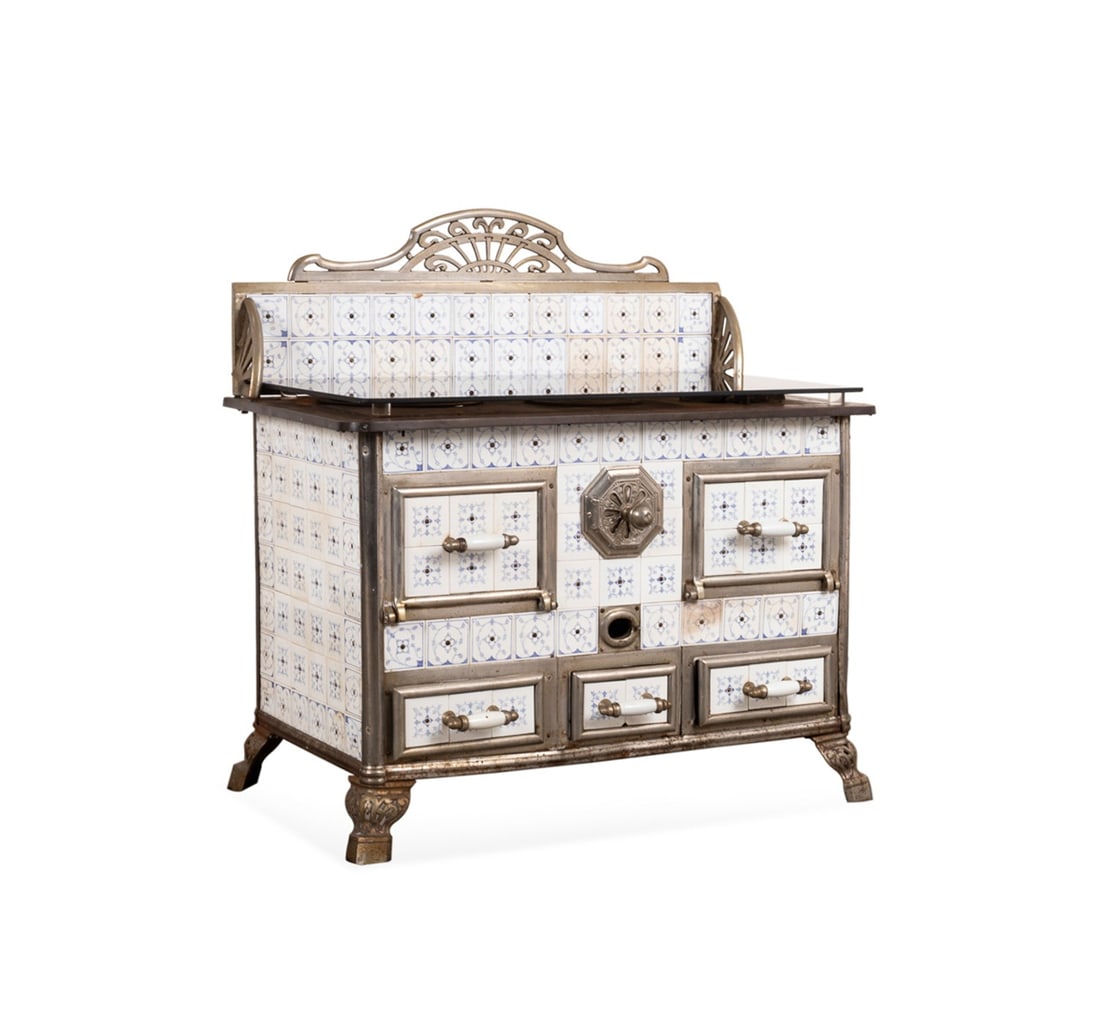 C. 1900 BELGIAN ART NOUVEAU TILED STOVE: Belgian, circa 1900. Art Nouveau tiled and nickel plated steel stove, having a pierced arched crest, blue and white tiles, two hinged doors over three drawers, and raised on pierced legs, apparently u