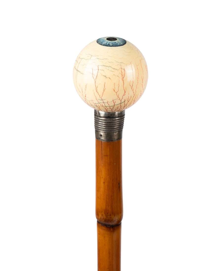 AMERICAN CARVED AND PAINTED EYEBALL WALKING CANE: American, circa 1910. Walking cane with bone sphere handle painted as an eyeball with iris, arteries, and veins, sterling silver collar, bamboo shaft, and metal ferrule. Approximate measurements: hand