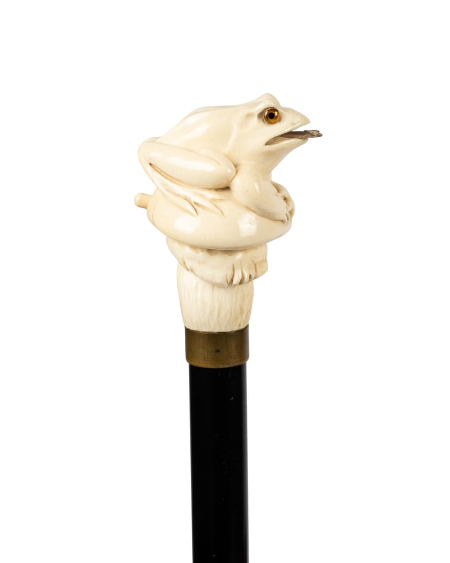 19TH C. ENGLISH SEATED FROG AUTOMATA CANE: English, circa 1890. Walking cane with fully seated frog on lily pad handle with button activated extending tongue showing fly, brass collar, ebonized hardwood shaft, and black horn ferrule. Approxima