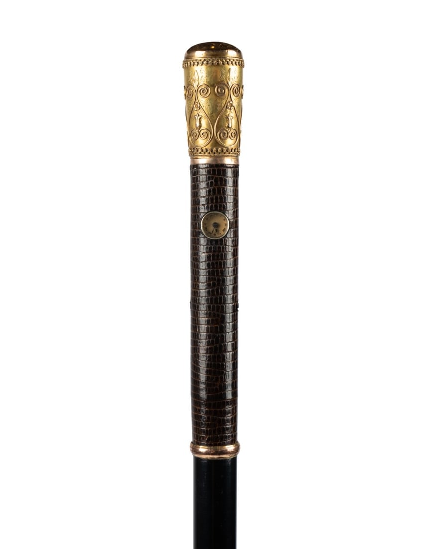 19TH C. AUSTRIAN HOLUSKA WATCH CANE: Austrian, circa 1885. Holuska watch cane with 18k yellow gold plated lizard handle decorated with raised floral and patterned designs, top engraved with Prince of Wales feathers, inset watch dial