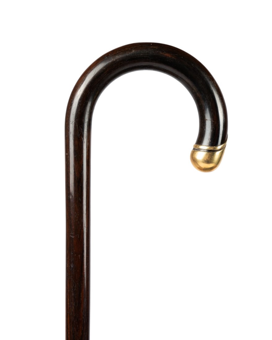 TIFFANY & CO 18K GOLD AND ROSEWOOD WALKING CANE: American, circa 1970. Tiffany & Company (American, founded 1839). Crook handle cane made of rosewood, 18k gold cap with an additional gold ring at the tip of the handle, shaft of rosewood ending at a