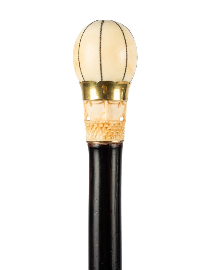 FRENCH HOT AIR BALLOON WALKING CANE, C. 1870: French, circa 1870. Walking cane with carved hot air balloon handle with full canopy and basket, gold dot at top, gold woven ropes, scalloped gold band marked "18k" and "MF", carved drapes and ropes,