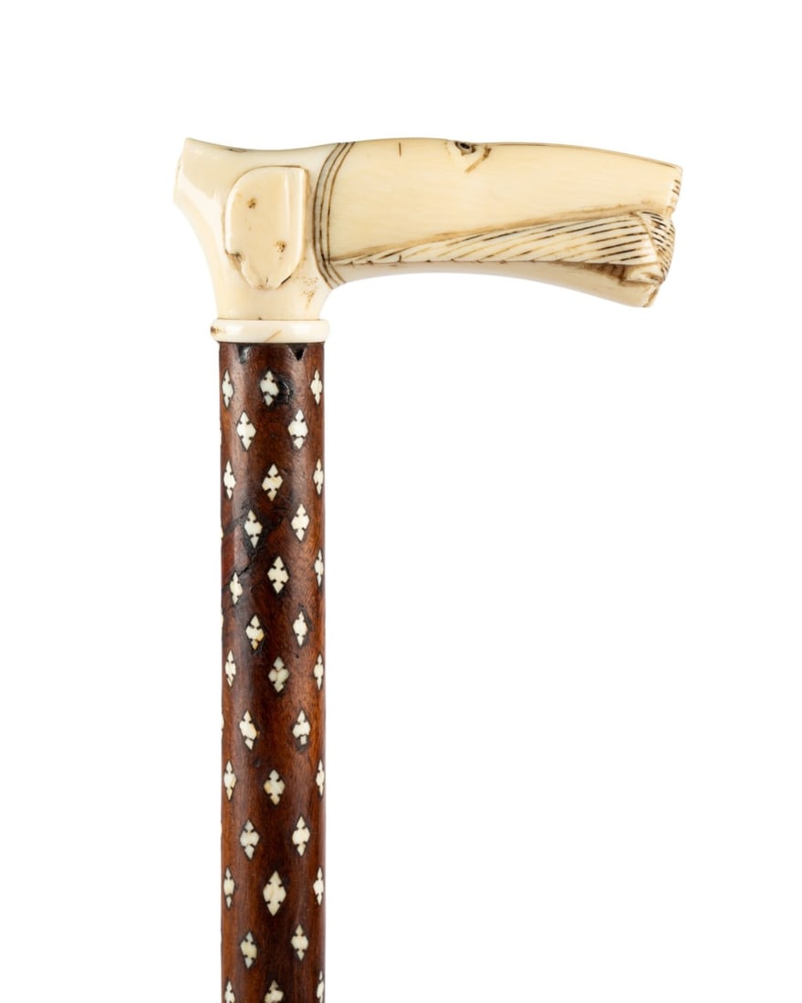 19TH C. ANGLO-INDIAN CARVED WALKING CANE: Indian, circa 1890. Anglo-Indian inlaid cane with a carved handle depicting a scene inspired by Sassanid sculpture, showing a wild animal holding a bird in its mouth, with heavily inlaid sandalwood