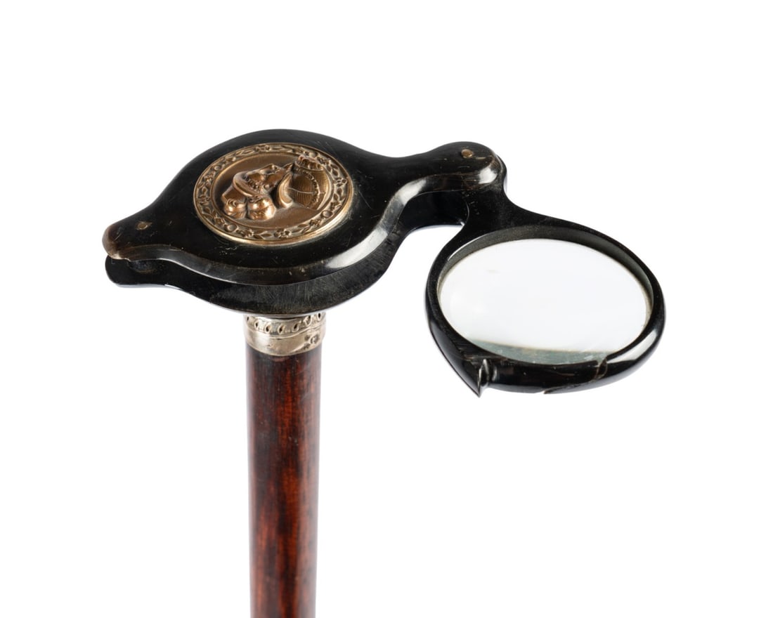 FRENCH FOLDING MAGNIFYING GLASS GADGET CANE: French, circa 1885. Cane with a horn folding magnifying glass handle with a nobleman bust in relief, shaft of stained exotic wood terminating at a horn ferrule. Approximate measurements: length: