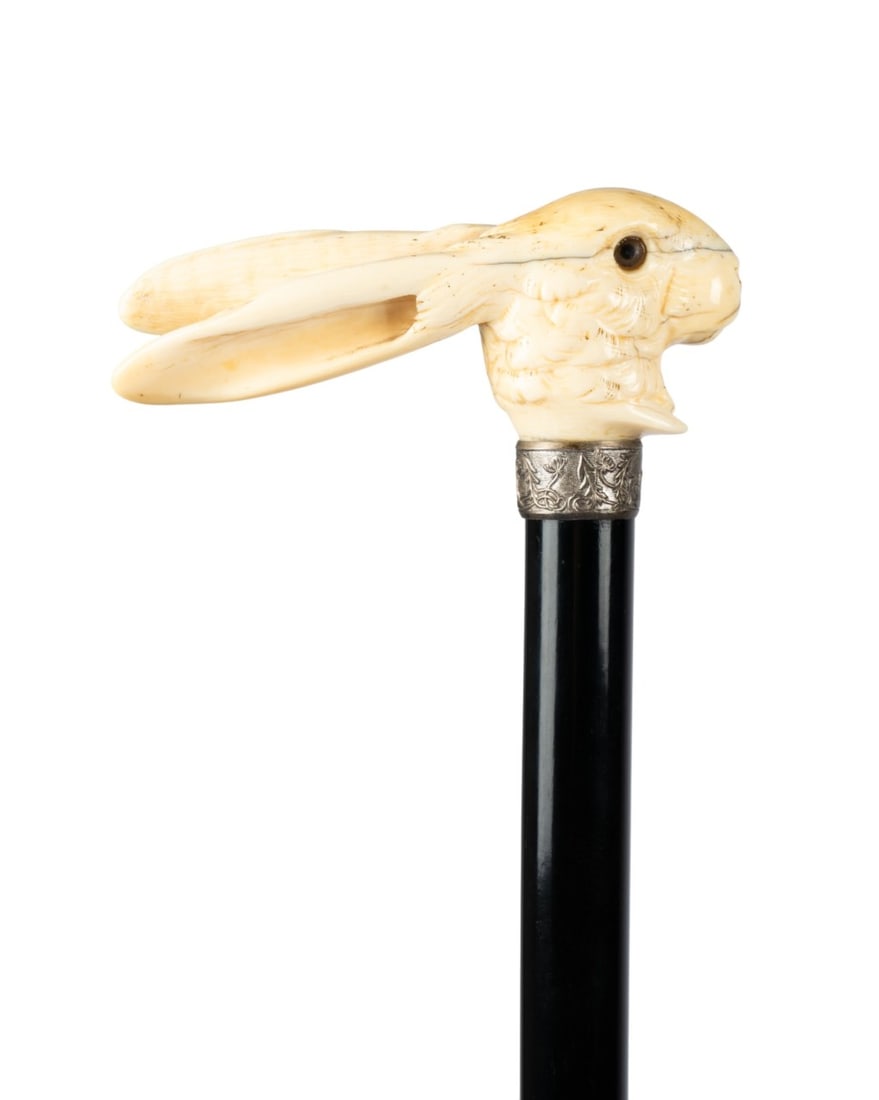 19TH C. ENGLISH RABBIT HANDLE WALKING CANE: English, circa 1870. Walking cane with carved bone rabbit handle with extended ears, silver collar, ebonized hardwood shaft, and horn ferrule. Approximate measurements: length: 35.5"