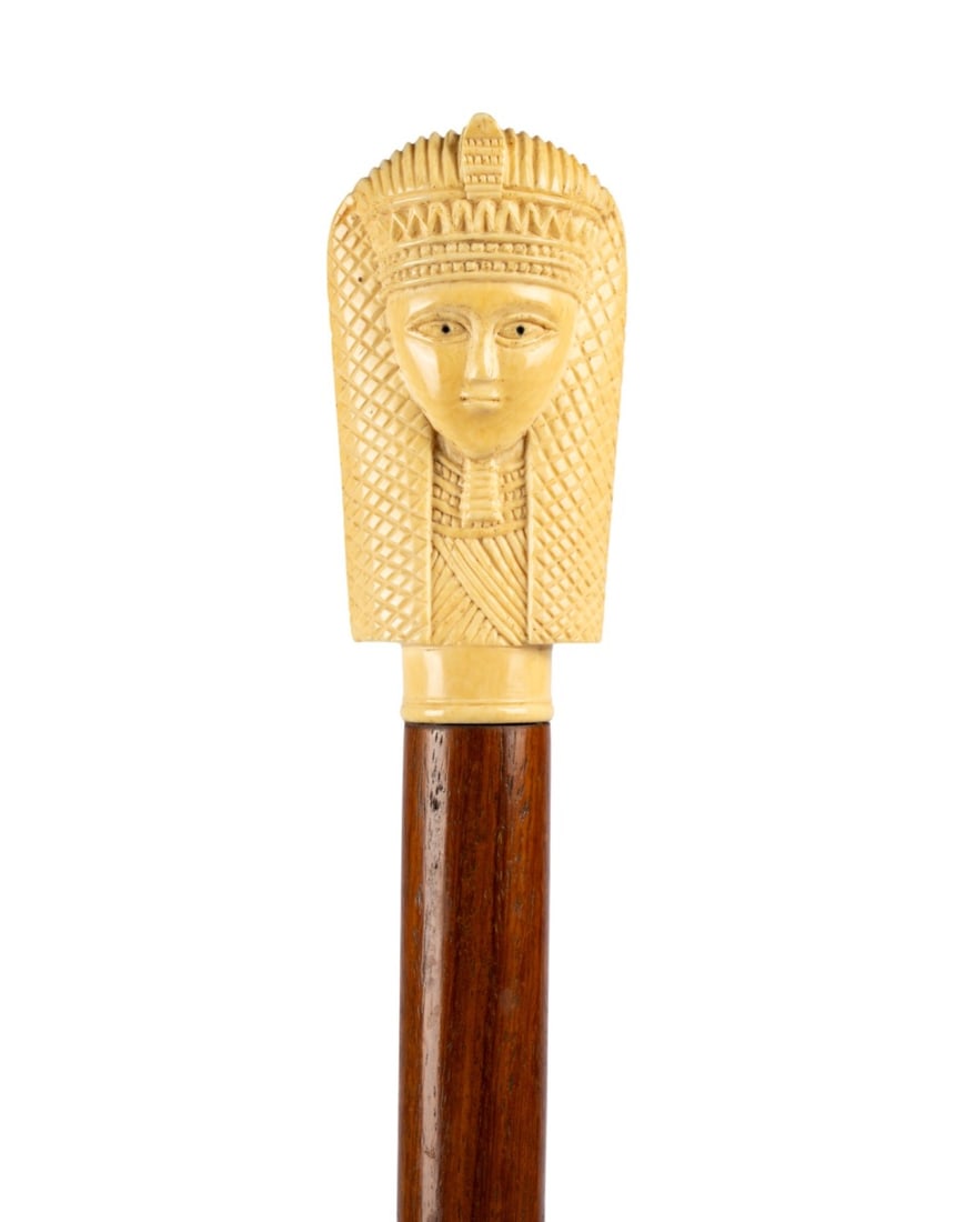 ANGLO-EGYPTIAN PHARAOH HEAD HANDLE CANE, C. 1900: Anglo-Egyptian, circa 1900. Walking cane with carved bone pharaoh head handle with elaborate headdress and snake, decorated front and back, bone collar, cherry wood shaft, and bone ferrule. Approximat