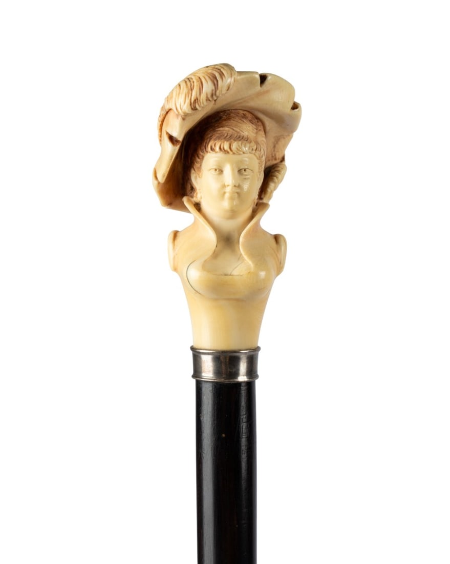 FRENCH GRANDE DAME BUST HANDLE CANE, C. 1880: French, circa 1880. Walking cane with carved handle of woman in Victorian dress and hat, silver collar, Macassar ebony shaft, and brass ferrule. Approximate measurements: handle: 3.25"; length: 36.5"