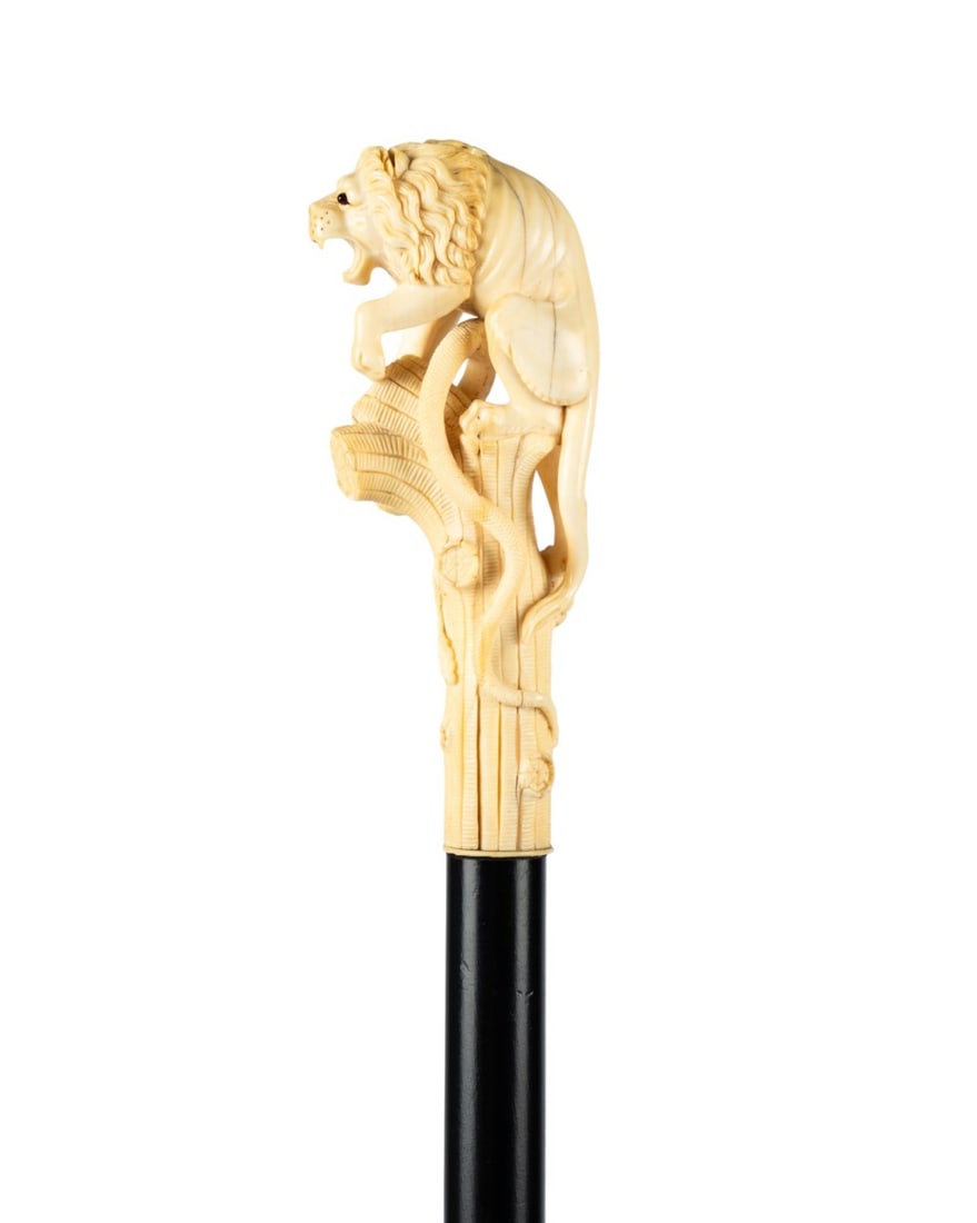 ENGLISH LION & SNAKE WALKING CANE, C. 1880: English, circa 1880. Walking cane with a carved handle depicting a lion atop an oak log with one foot on the head of a snake, the lion detailed with a bushy mane, snarling pose, and two dark glass eye