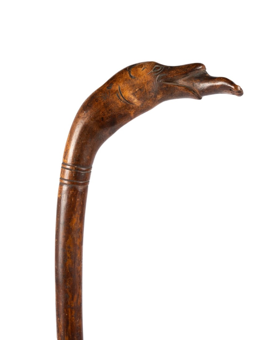 19TH C. AMERICAN FOLK ART CARVED WOOD CANE: American, circa 1880. Folk art cane carved from a single piece of hardwood, with carved handle depicting an unusual animal with duck bill and human foot protruding from its mouth, natural oval depress