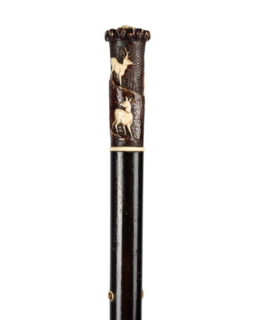19TH C. ENGLISH DEER & DOG WALKING CANE: English, circa 1860. Deer motif cane with carved handle with three raised deer and a hunting dog in relief, attached to dark stained hardwood shaft by wooden screw with hole at top for string, and bon