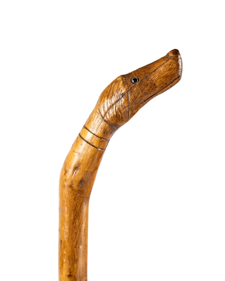 ENGLISH FOLK ART DOG HANDLED WALKING CANE, C. 1890: English, circa 1890. Walking cane with carved dog head handle with inset glass eyes, maple handle and shaft slightly bowed in spots, and no ferrule. Approximate measurements: length: 38.75"