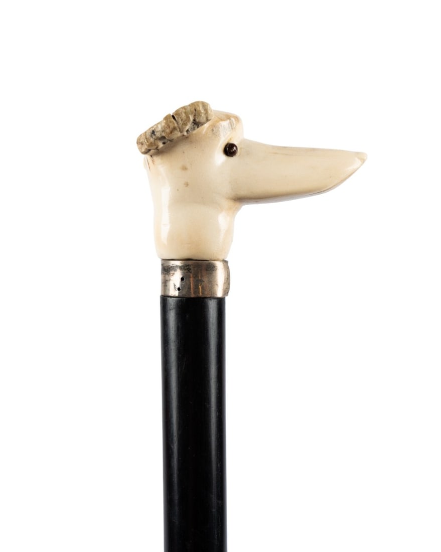 19TH C. ENGLISH DOG HEAD WALKING CANE: English, circa 1880. Walking cane with stylized carved dog head handle with inset glass eyes and short alert ears, silver collar, ebonized hardwood shaft, and horn ferrule. Approximate measurements: h