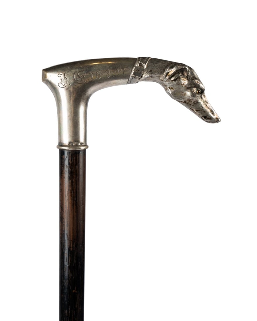 SILVER WHIPPET DOG HEAD HANDLE CANE, C. 1907: Austro-Hungarian, circa 1907. Walking cane with silver handle shaped as a whippet with inset glass eyes, smooth handle engraved ?DF 16-3-07,? silver marked 800 with Vienna hallmark, connecting to ebon
