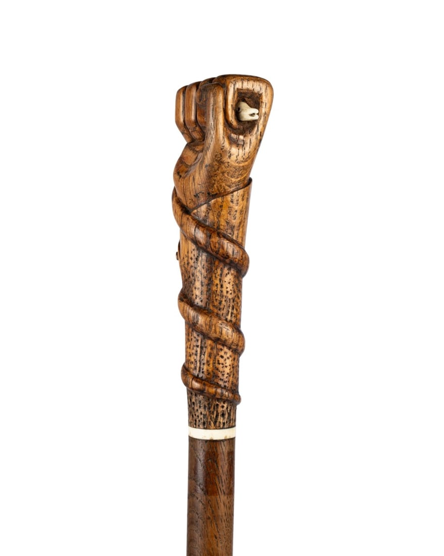 ENGLISH SNAKE IN FIST HANDLED CANE, C.1895: English, circa 1895. Walking cane with carved fruitwood fist handle entwined by a snake with head on one side and coiled body on the other, bone collar, hardwood shaft, and metal ferrule. Approximate