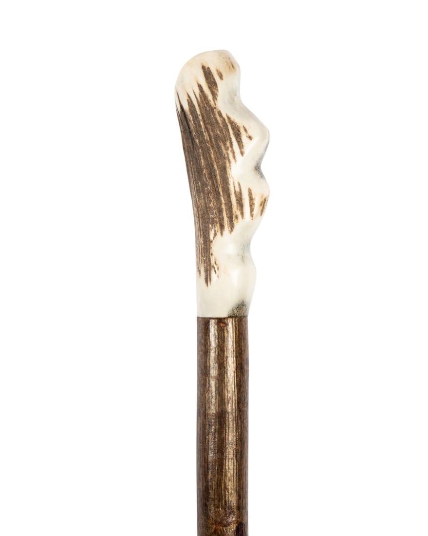 CARVED BONE HIKING CANE, C. 1920: Continental, circa 1920. Hiking cane with carved handle stained for depth, stained oak shaft with attached leather tassel, and steel ferrule. Approximate measurements: handle: 4.25"; length: 55"