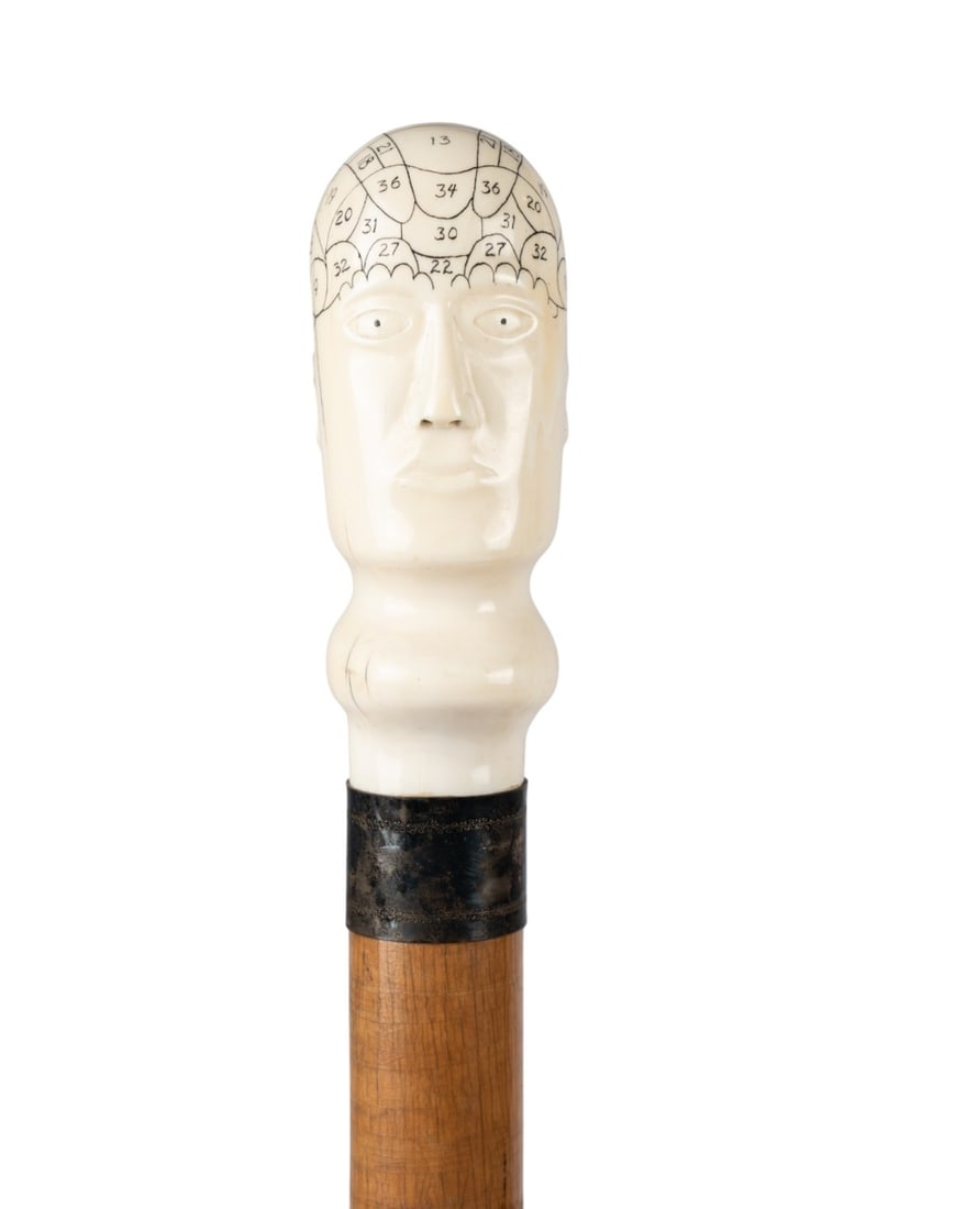 ENGLISH PHRENOLOGY HEAD HANDLED CANE, C. 1840: English, circa 1840. Walking cane with carved bone phrenology head handle numbered 1-36, embossed silver collar, tropical wood shaft, and horn ferrule. Approximate measurements: length: 38.5"