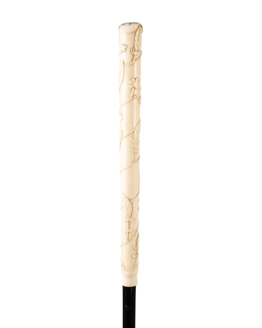 GERMAN CARVED BONE LONG HANDLED CANE, C. 1860: German, circa 1860. Walking cane with carved bone handle comprising nearly a third of the cane, leaf and flower designs with pique detail at top, ebony shaft, and bone ferrule with nail at tip. Approx