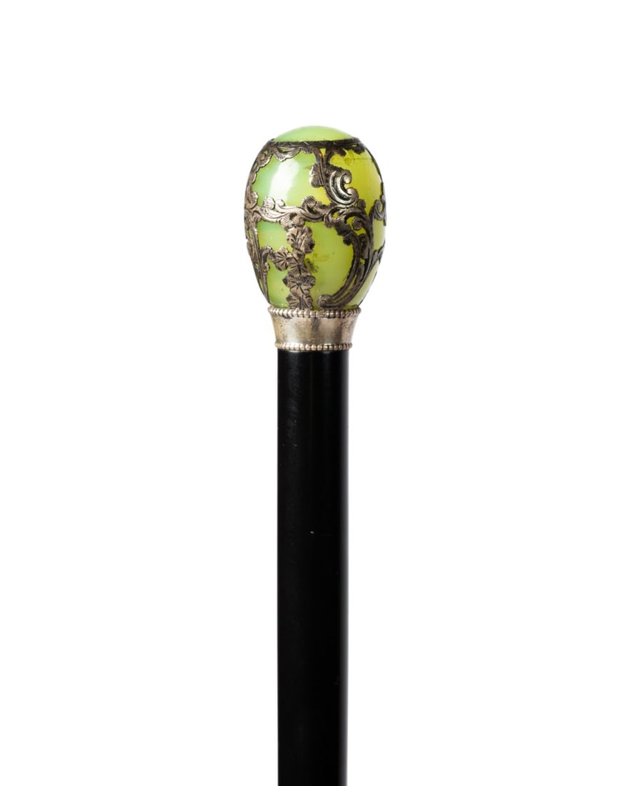 JADE & SILVER OVERLAY DRESS CANE, C. 1890: Continental, circa 1890. European cane with an egg-shaped green jade handle with silver overlay in a decorative foliate style, supported by a small silver collar, connected to an ebonized hardwood