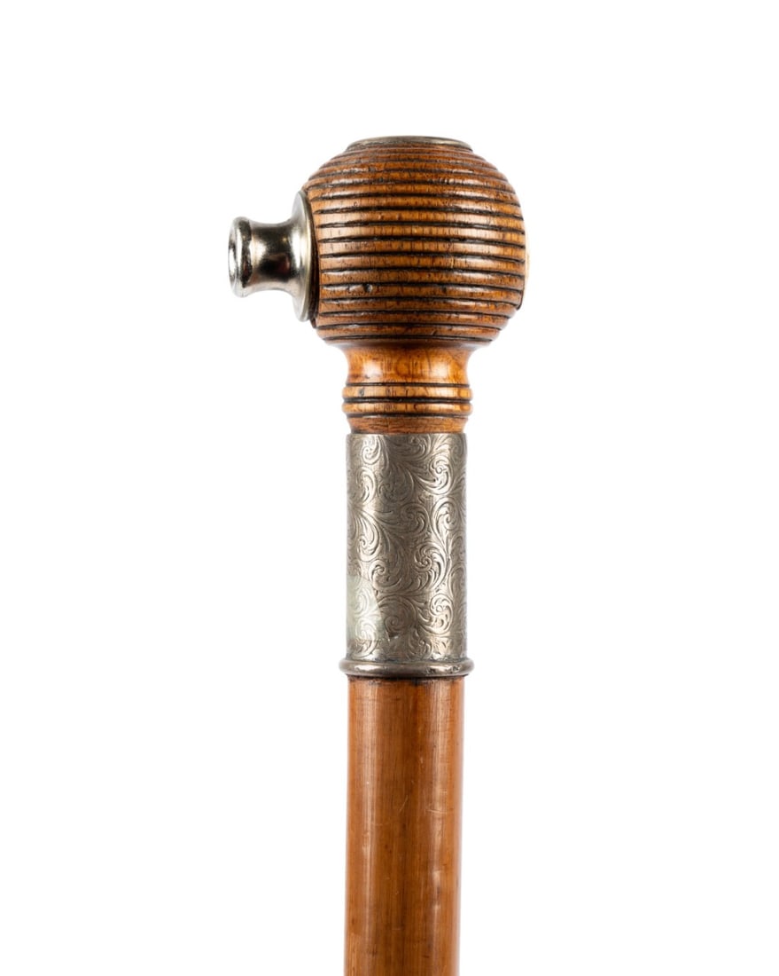 ENGLISH NOISEMAKER WALKING CANE, C. 1910: English, circa 1910. Cane with a round ribbed ball handle incorporating a metal mouthpiece and vent that produces a siren sound when blown, with an engraved silver scrollwork collar, a Malacca shaft,