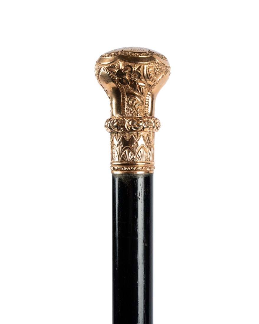 AMERICAN GILT HANDLED PRESENTATION CANE, 1906: American, 1906. Walking cane with very ornate gilt top with flowers and botanicals on the side, cartouche at the top engraved "Presented to M. Beatty by Roommates, March 29, 1906," with ebony shaft te
