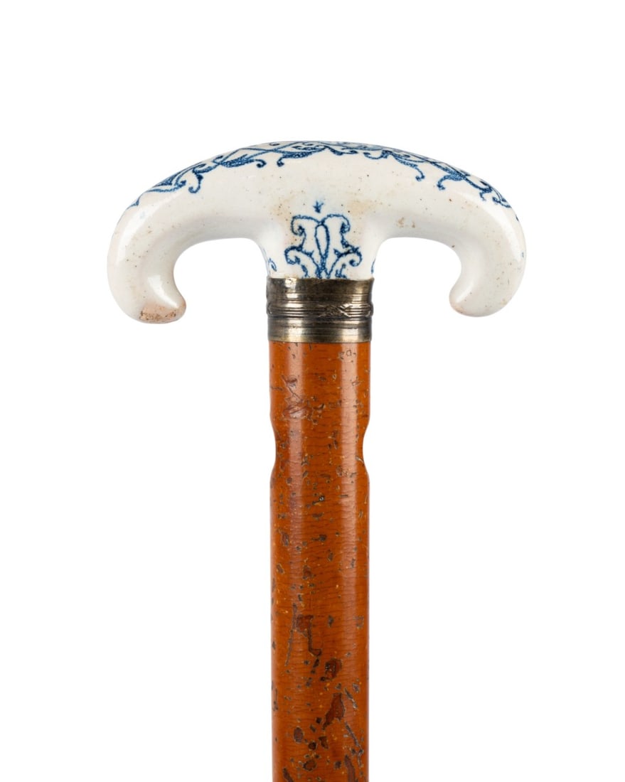 BLUE AND WHITE EARTHENWARE WALKING CANE, C. 1820: French / Belgian, circa 1820. Walking cane with blue and white earthenware handle decorated with a stylized face in the manner of Delft, supported by a brass collar, with Malacca wood shaft pierced