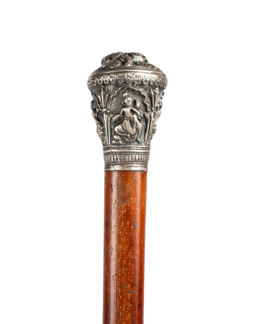 THAI DANCING GODDESSES WAKLING STICK, C. 1890: Thai, circa 1890. Walking cane with silver knob handle decorated with lion at top and four dancing goddesses in archways on sides, with full bark Malacca shaft terminating in metal ferrule. Approximat
