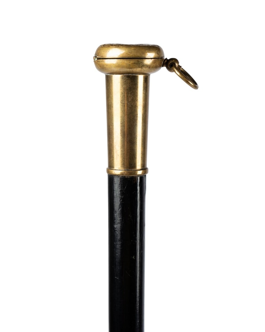 19TH C. ENGLISH COIN HOLDER GADGET CANE: English, circa 1880. Gadget walking cane with brass top opening to reveal dime-sized coin holder, supported by brass collar, with ebonized hardwood shaft terminating in brass ferrule. Approximate meas