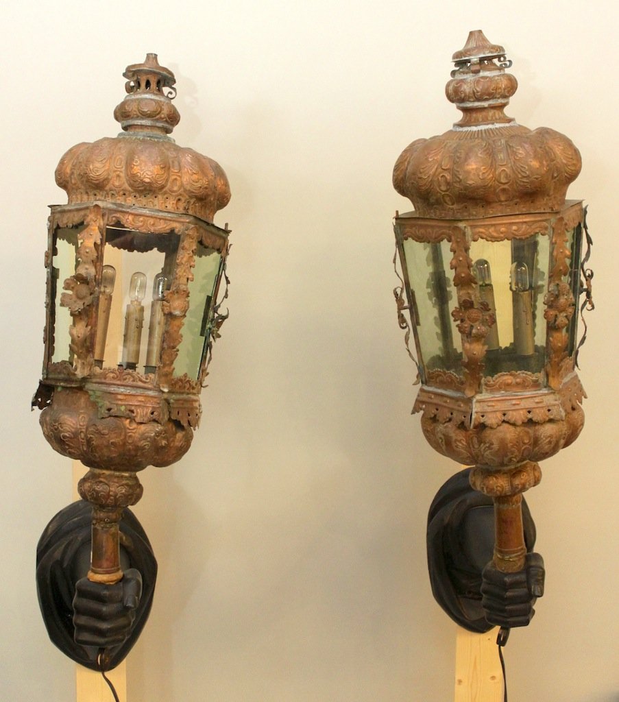 Pair of Copper Lanterns In Blackamoor Style: Carved Wooden Fist Holding Ornate Copper Lanterns With Individual Glass Panels. Lighted. Lanterns measure 3 feet high. Bracket measures 14"H x 9"W. Entire fixture is 2 feet deep.