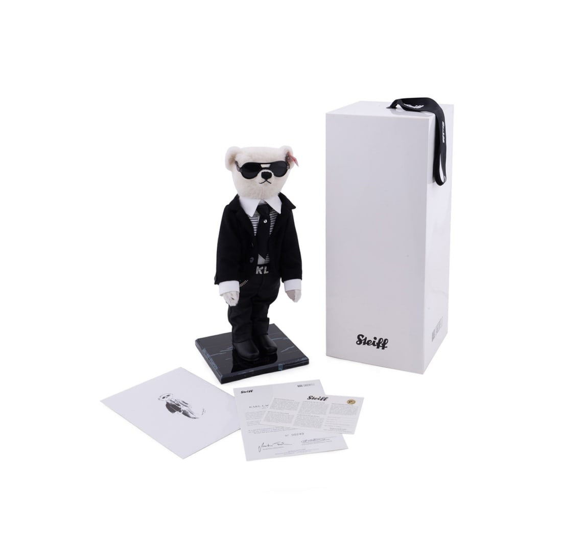 KARL LAGERFELD STEIFF TEDDY BEAR IN ORIGINAL BOX: Karl Lagerfeld for Steiff (German, founded 1880). Stuffed teddy bear dressed in outfit with sunglasses, rhinestone belt bucket, with stand, appropriately marked. Accompanied by original box. Provenanc