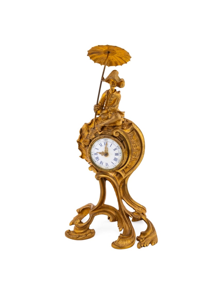 FRENCH LOUIS XV REVIVAL MANTEL CLOCK: French, late 19th century. Chinoiserie ormolu mantel clock in the rococo manner topped with a figure holding an umbrella, an enameled face with black roman numerals, scrolled feet with shells, key wou