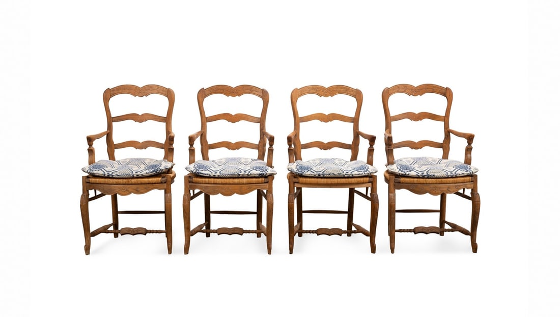 FOUR FRENCH PROVINCIAL RUSH SEAT DINING ARM CHAIRS: French. Set of four Provincial style dining arm chairs, having three shaped rails, over a rush seat with a floral carved apron, and raised on front cabriole legs with scroll feet, apparently unmarked.