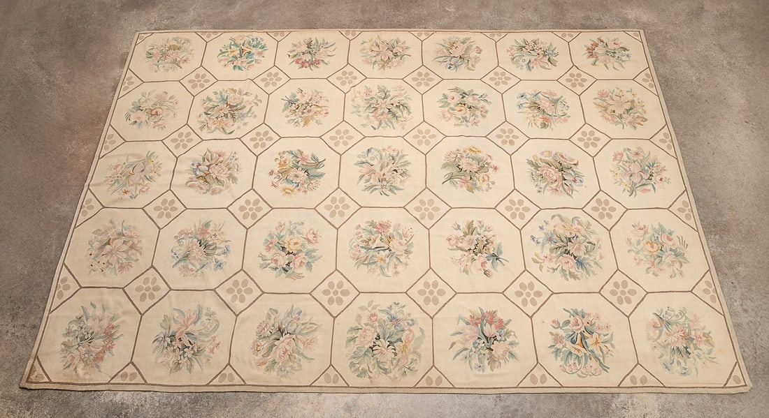 NEEDLEPOINT FLORAL RUG: American, 20th century. Needlepoint floral motifs set in a geometric pattern, having pink, blue, yellow, and green, and taupe accent colors on a bone field. Provenance: Estate of Scott Hudgens and Jac