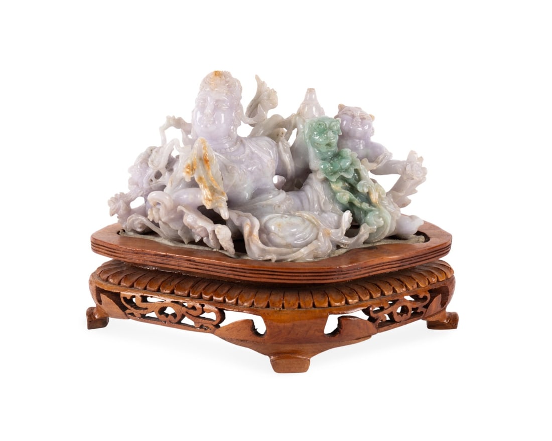CHINESE JADE CARVING OF THE BODHISATTVA: Chinese, 20th century. Pale green and lavender jade carving of a reclining goddess of mercy surrounded by exotic and mythological beast, on a carved wooden stand, apparently unmarked. Provenance: Priv