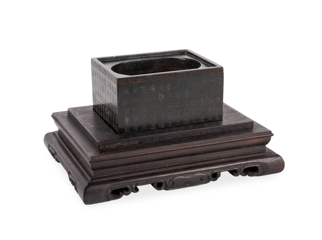 CHINESE INKSTONE AND CASE: Chinese, 19th century. Large inkstone carved with Chinese characters surrounding all four sides, having carved box lid, accompanied by wooden stepped carved stand. Approximate dimensions: h. 2.5", w.