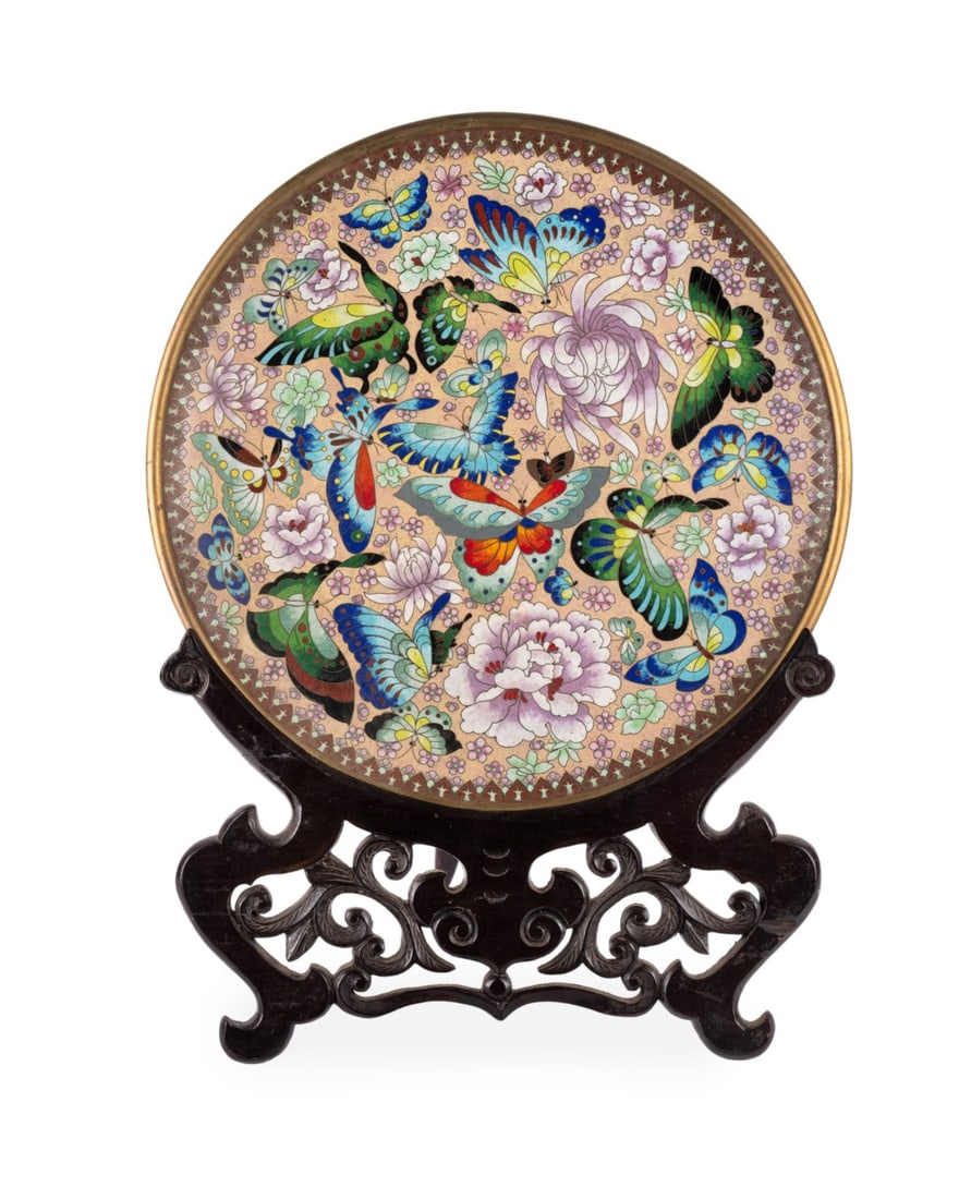 CHINESE CLOISONNE BUTTERFLY MOTIF CHARGER: Chinese, early 20th century. Large cloisonne charger featuring several multicolor butterflies surrounded by pale pink peonies and mums, encircled by a sawtooth border, presented on a wooden carved sta