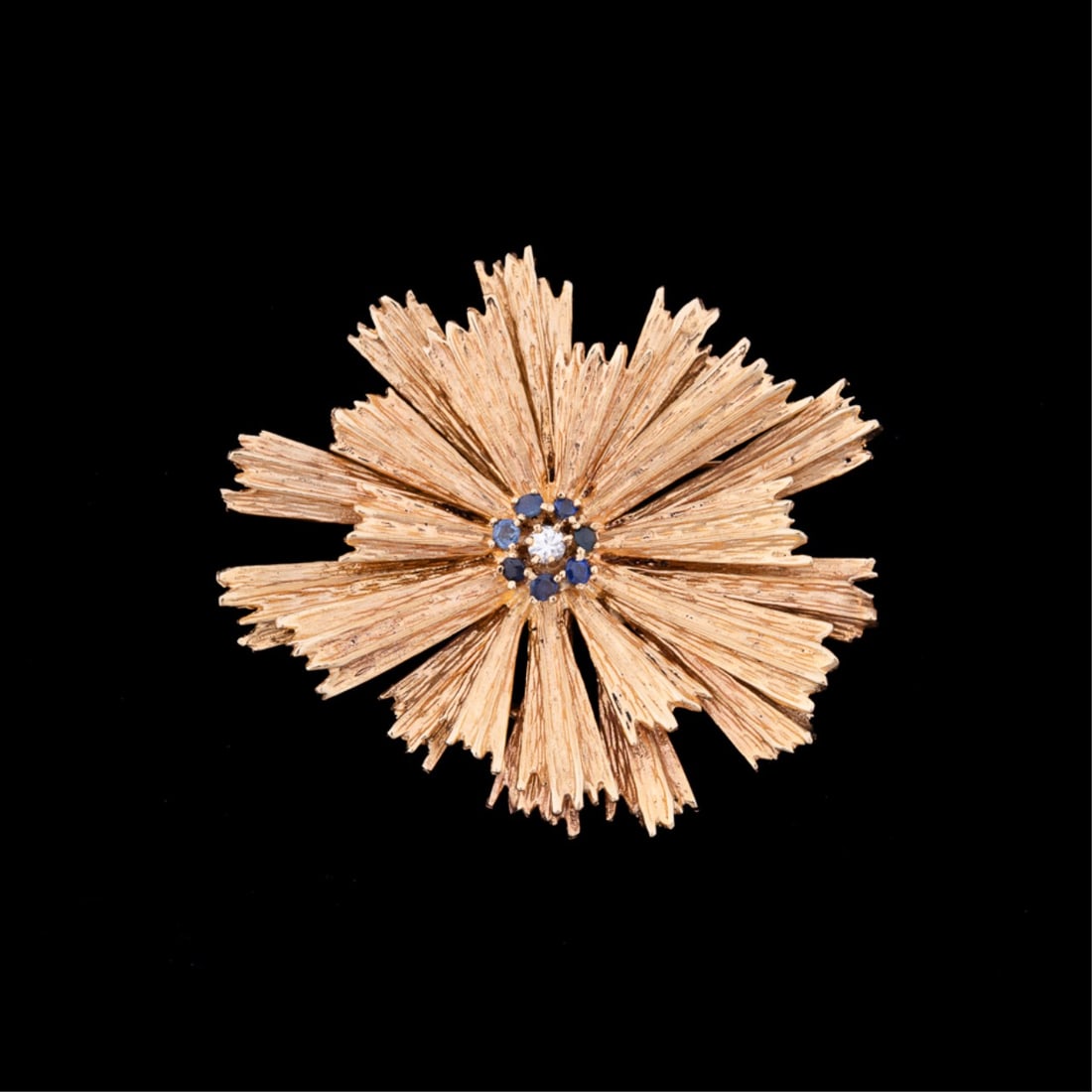 SAPPHIRE, DIAMOND & 14K YG STARBURST BROOCH: Sapphire, diamond, and 14k yellow gold starburst form brooch centering on a round cut diamond weighing approximately 0.10 total carats and surrounded by (7) round cut sapphires measuring approximately