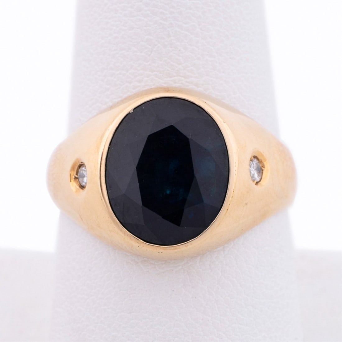 OVAL SAPPHIRE AND DIAMOND RING, BEZEL SET 14K YG: Sapphire and diamond ring featuring (1) oval shape dark blue sapphire weighing approximately 5.25 total carats accented by (2) round brilliant cut diamonds weighing approximately 0.08 total carats. Be