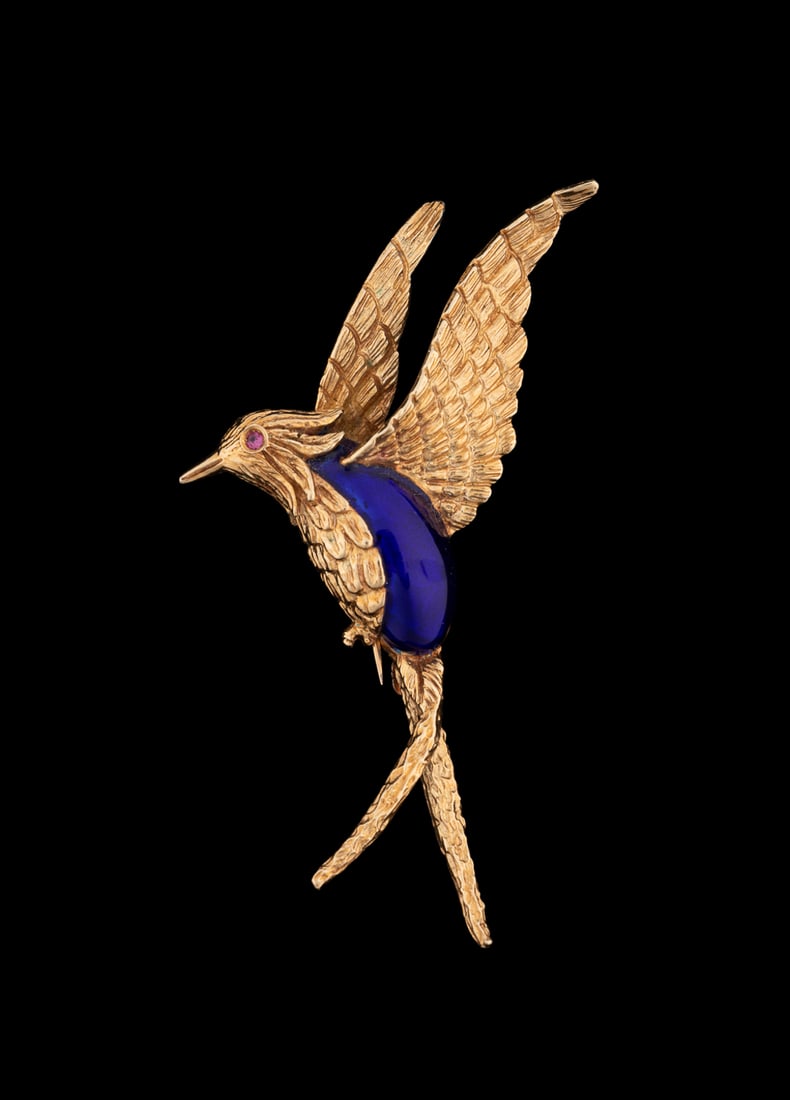 18K Yellow Gold and Blue Enamel Hummingbird Pin: Textured yellow gold Hummingbird in flight, accented by blue enamel body and round cut ruby eye. Stamped '18K MP'. Approximate dimensions: Length: 2 1/2 in.Width: 1 3/4 in.7.13 grams Provenance: Priva