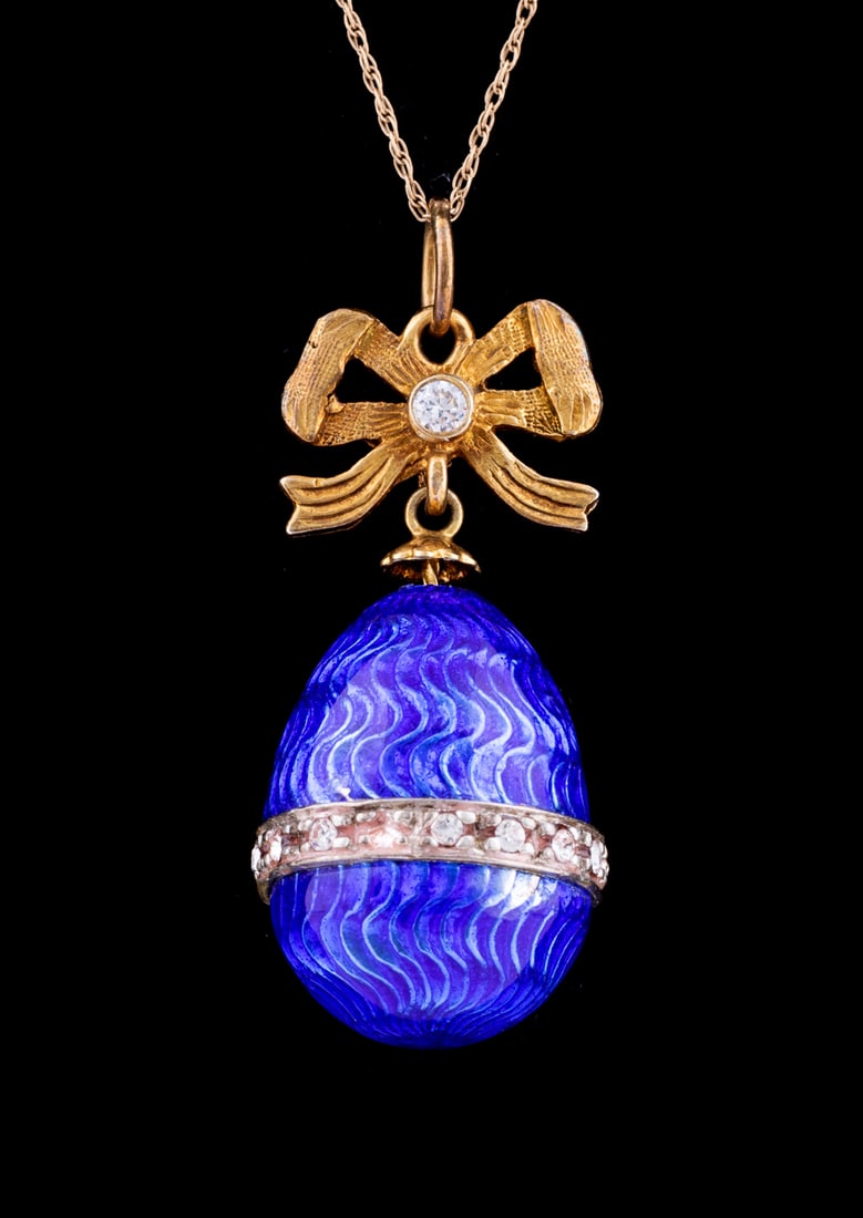 Blue Enamel Egg Pendant Necklace: Pendant featuring a guilloche blue enamel egg accented by a silver toned metal band of round cut colorless glass, suspended from a yellow gold toned bow accented by a single round cut colorless glass,