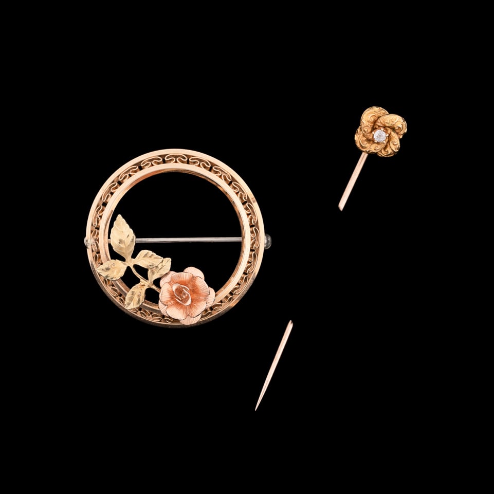 Two 14 Karat Gold Pins: One Krementz openwork yellow gold circle pin accented by rose and yellow gold rose bud, and a yellow gold stick pin of sculptural engraved rosette form centering on a single round cut diamond. Circle 