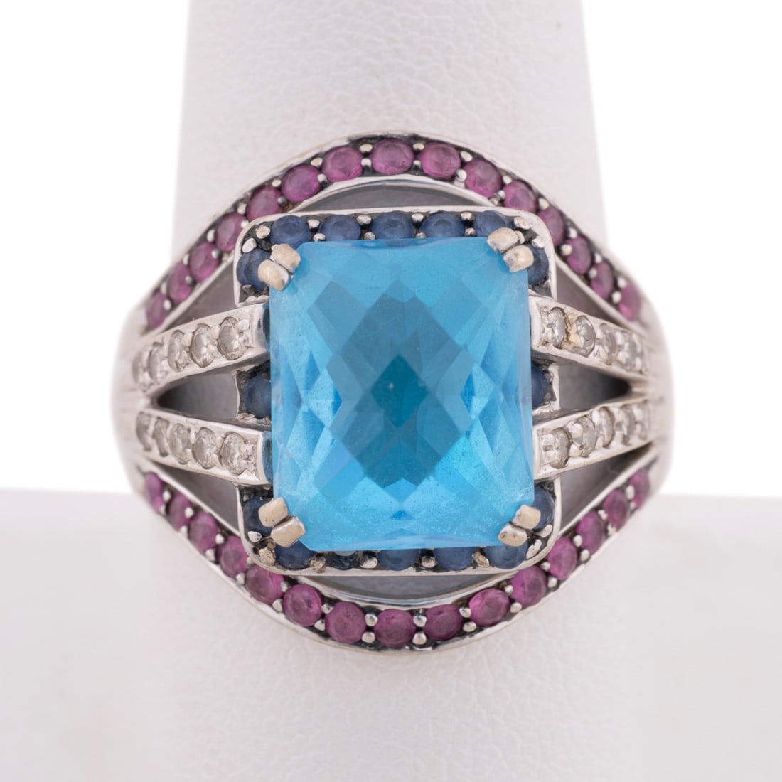 Ruby, Sapphire & Topaz 18K White Gold Ring: With a central cushion cut checkerboard faceted blue topaz measuring approximately 11.84 x 9.98 x 6.58mm, (30) round rubies, each approx. 1.5mm; (15) round dark blue topaz, each approx. 1.5mm and (20)