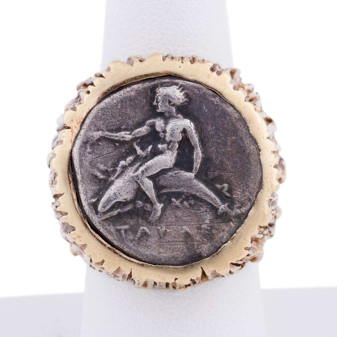 18K Yellow Gold Greek Coin Ring: Centering on a ancient-style silver toned Greek coin depicting a man riding a dolphin set in textured yellow gold band. Stamped '18K' and illegible maker's mark. Approximate dimensions: Ring size: 9 1