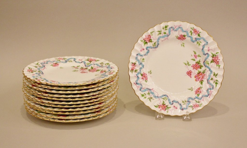 12 English Montrose Plates.: With hand painted pink flowers and blossoms and blue ribbon. Gold accented rim on scalloped edges. Marked on bottom with "MONTROSE ENGLAND" and with logo in fuchsia. Embossed MINTON CHINA.