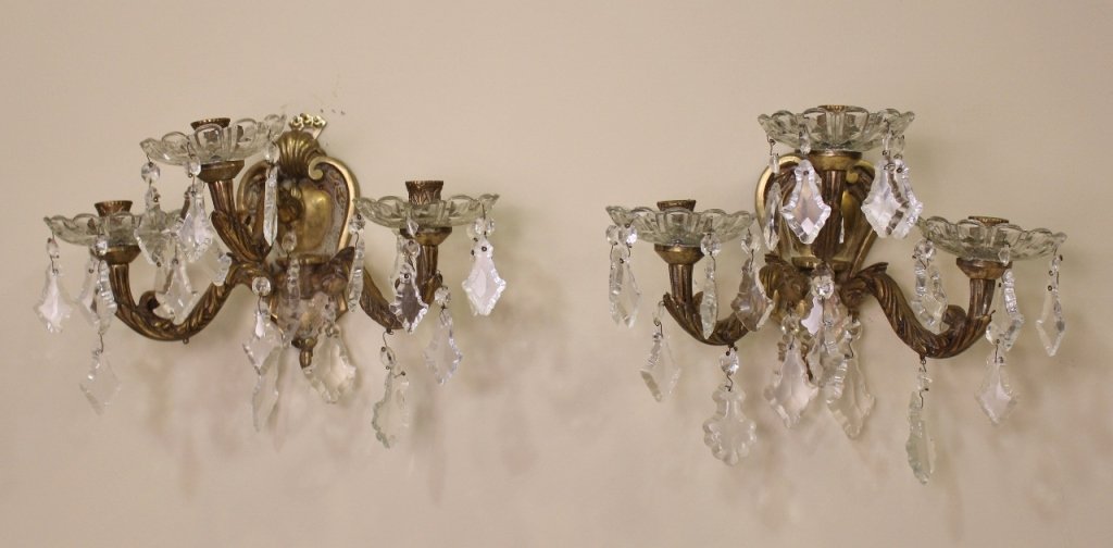 Pair of Crystal Sconces: Pair of matching wall sconces with three arms terminating to candle holders (one above and two below). Wall sconces with shell and foliate decoration on metal with clear crystals hanging from arms. Wa